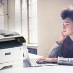 Xerox® B315 multifunctionele printer in werksituatie Jonge vrouw die op haar computer werkt naast een Xerox® B315 multifunctionele printer.