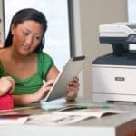 Xerox® VersaLink® B415 multifunctionele printer op de werkplek Twee vrouwen gebruiken een tablet voor een Xerox® VersaLink B415 multifunctionele printer