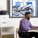 Xerox® VersaLink® C415 multifunctionele kleurenprinter in een kantoor Mannen werken op een laptop voor een Xerox® VersaLink® C415 multifunctionele kleurenprinter