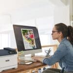 Een vrouw zit aan een bureau, gefocust op haar werk, met een Xerox® C320 kleurenprinter Een vrouw zit aan een bureau, gefocust op haar werk, met een Xerox® C320 kleurenprinter