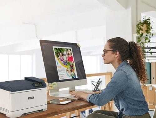 Een vrouw zit aan een bureau, gefocust op haar werk, met een Xerox® C320 kleurenprinter