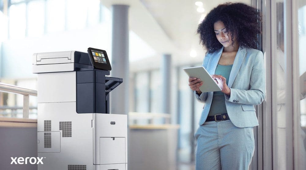 Xerox® ConnectKey®: mobiele connectiviteit Een persoon staat naast een Xerox VersaLink B605 multifunctionele printer en kijkt naar een tablet. Hij communiceert met deze tablet, wat illustreert hoe ConnectKey mobiele interactie met de printer mogelijk maakt.