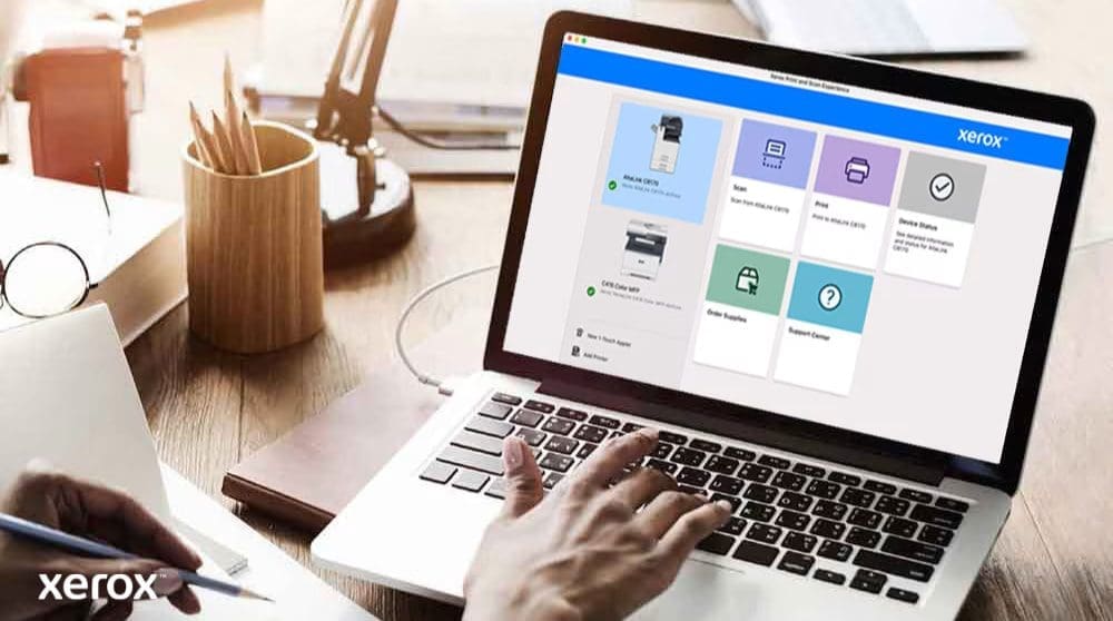 Xerox® Print- en scanervaring: intuïtieve bediening Iemands handen liggen op het toetsenbord van een laptop en op het scherm wordt de interface van Xerox Print and Scan Experience weergegeven, met opties zoals Scannen, Afdrukken, Apparaatstatus, Benodigdheden bestellen en Ondersteuningscentrum, wat wijst op een gebruiksvriendelijke bediening.