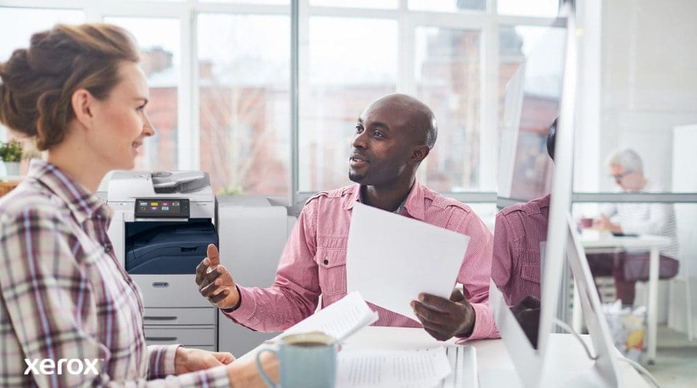 Xerox® Workplace Cloud et Suite : gestion centralisée du parc Une personne examine des données sur l'écran d'un ordinateur portable, avec une superposition numérique de diverses icônes d'appareils (imprimantes, appareils mobiles) et de lignes connectées, symbolisant la gestion centralisée de la flotte pour Xerox Workplace Solutions.